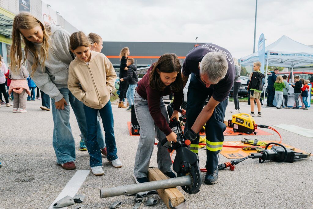Mädchen schneidet mit der Bergeschere ein Metallrohr, ein Feuerwehrmann hilft