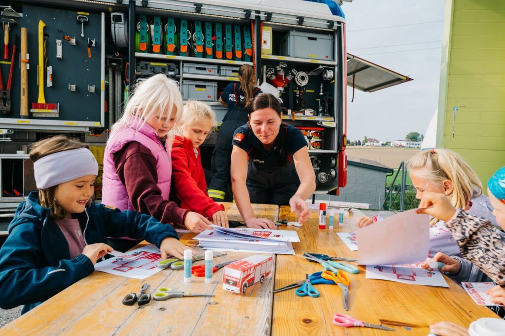 Kinder basteln vor dem Feuerwehrauto ein Feuerwehrauto aus Papier
