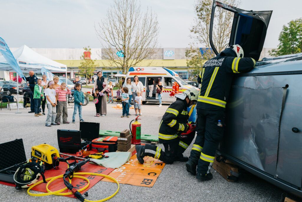 Feuerwehrleute arbeiten an einem umgekippten Auto, Kinder schauen zu