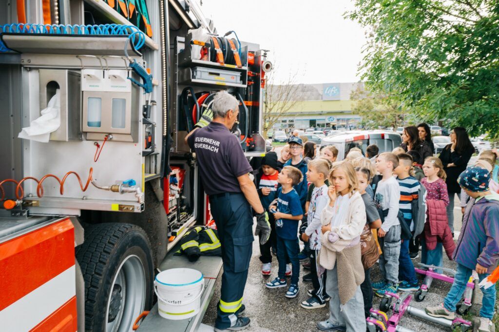 Feuerwehrmann erklärt Schulkindern die Ausrüstung am Feuerwehrauto