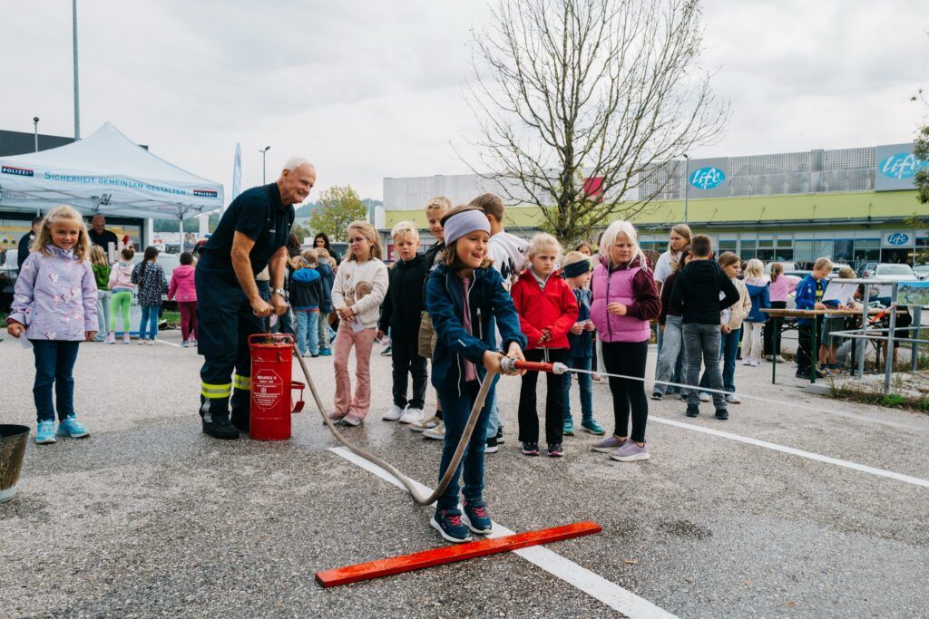 Mädchen spritzt mit dem Feuerwehrschlauch, andere Kinder warten in der Reihe