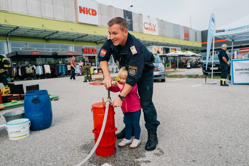 Polizist hilft einem kleinen Kind an der Kübelspritze